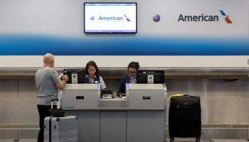 Two workers help a passenger at an American Airlines kiosk inside of an airport.