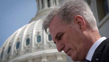 A side-profile photo of the face of House Speaker Kevin McCarthy. In the background is the U.S. Capitol.