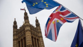 EU and Union Jack flags waving outside of the Houses of Parliament in London.