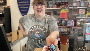Lindsay Farrell smiles widely and holds out a 100-sided die.
