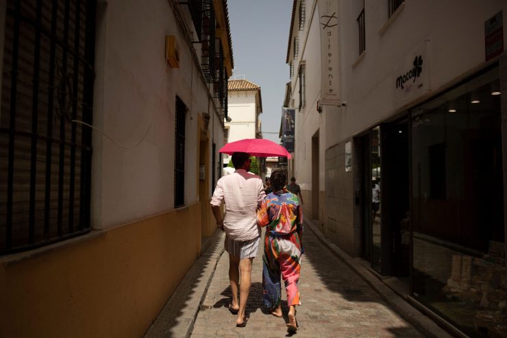 Los turistas se protegen del sol con una sombrilla mientras caminan por una estrecha calle española.