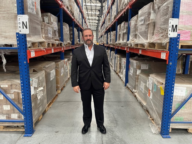 Guillermo Fernández de Jáuregui se encuentra en un almacén.  Está rodeado de estanterías industriales llenas de cajas.