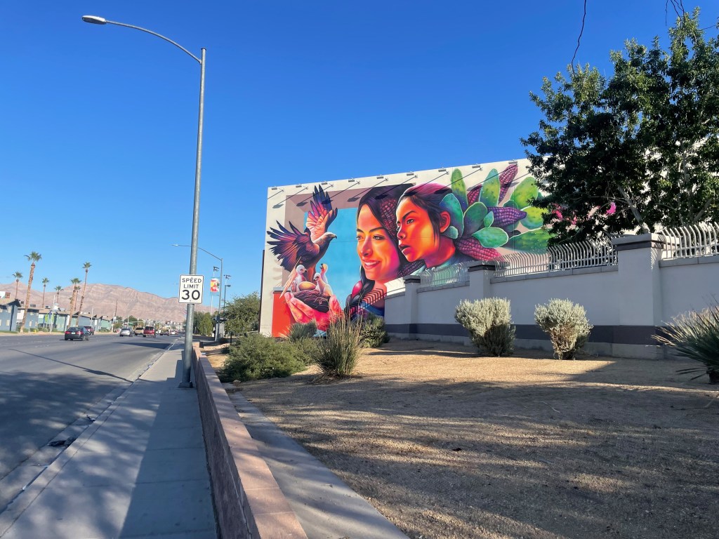 A multicolored mural dedicated to the immigrant experience near the side of a road.
