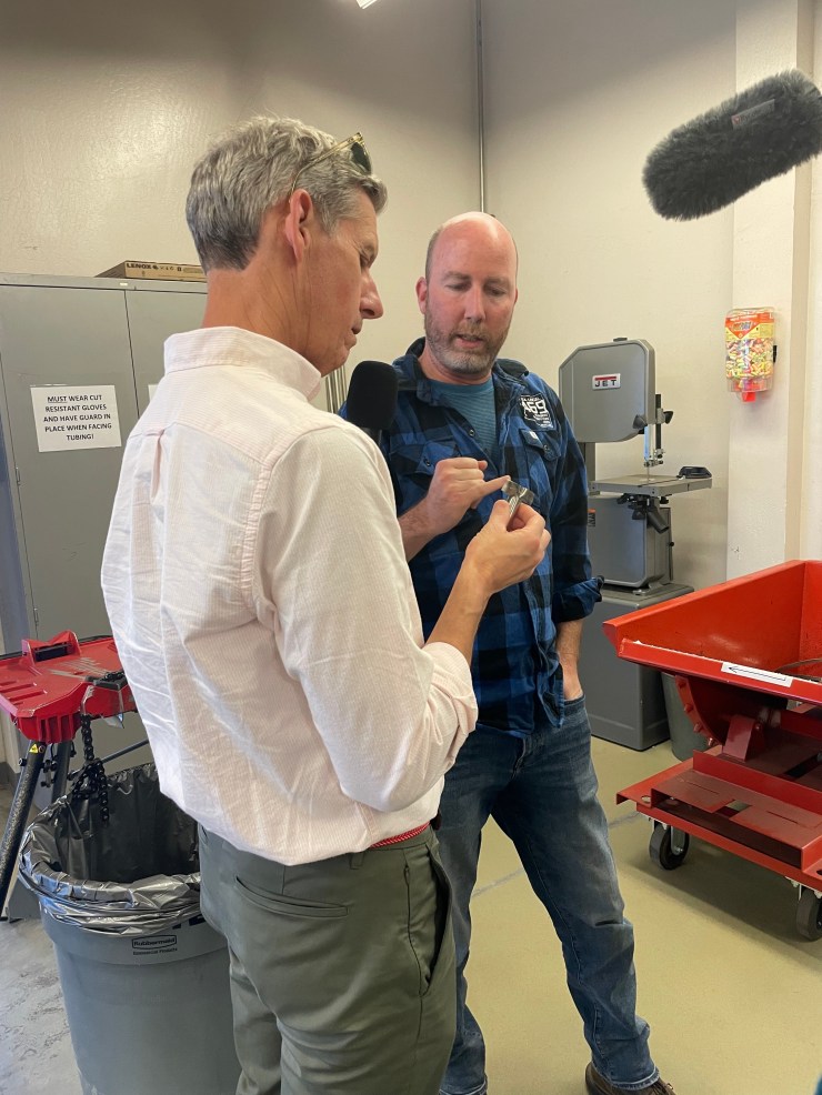 Marketplace's Kai Ryssdal speaks with Travis Laid, assistant training director for Arizona Pipe Trades, the local pipefitters union.  Ryssdal wears a white button-up with gray pants.  Laid is wearing a blue and black flannel and blue jeans.
