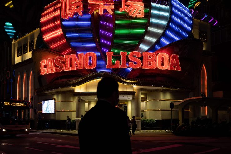 People walk past the Casino Lisboa, which is lit up in neon lights at night.