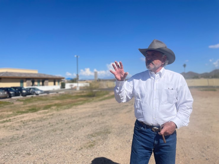 Eckert, in a cowboy hat, stands on an empty stretch of land.