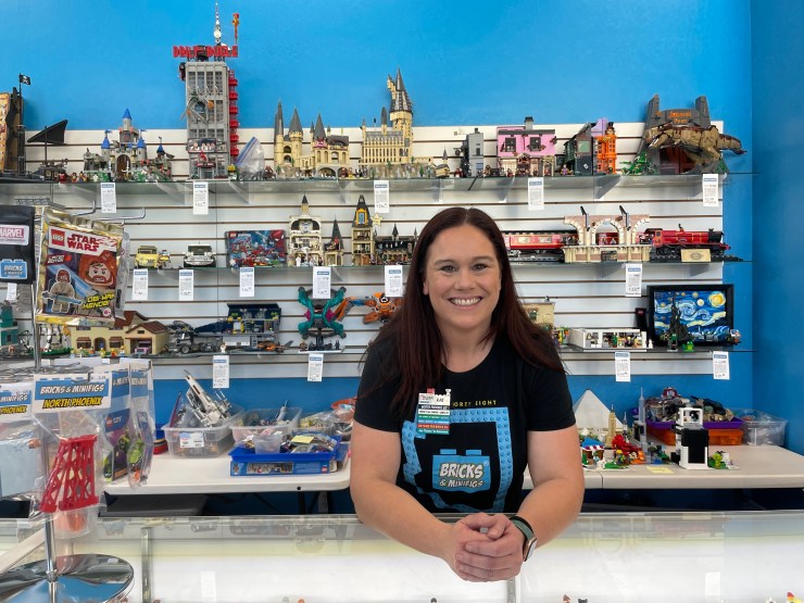 Blaz smiles from behind the counter of her store. Behind her is a display of Lego models.